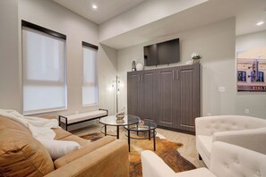 Un salon moderne avec un canapé, des fauteuils, une table basse et un téléviseur à écran plat fixé au mur.