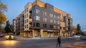 A multi-story building with a modern design, featuring a mix of glass and wood paneling, and a ground-level commercial space. - Downtown Luxury Loft | Extreme Walkability (Bozeman)