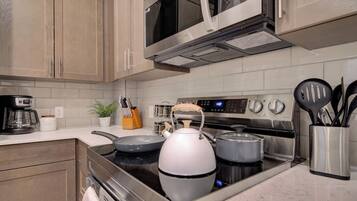 A modern kitchen with stainless steel appliances, including a stove, microwave, and oven. There are pots and pans on the stove, and a kettle on the counter.
