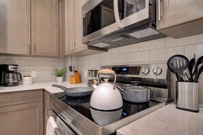 Une cuisine moderne équipée d’appareils électroménagers en acier inoxydable, notamment une cuisinière, un four à micro-ondes et un four traditionnel. On peut voir des casseroles et des poêles sur la cuisinière, et une bouilloire sur le plan de travail.
