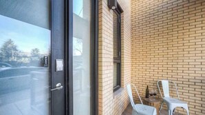 A balcony with two white chairs, a small table with a bottle and glasses, and a brick wall. - Downtown Luxury Loft | Extreme Walkability (Bozeman)