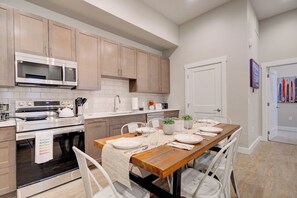 Une cuisine moderne avec des meubles en bois, un four à micro-ondes en acier inoxydable et un coin repas avec une table en bois, mise pour quatre personnes.