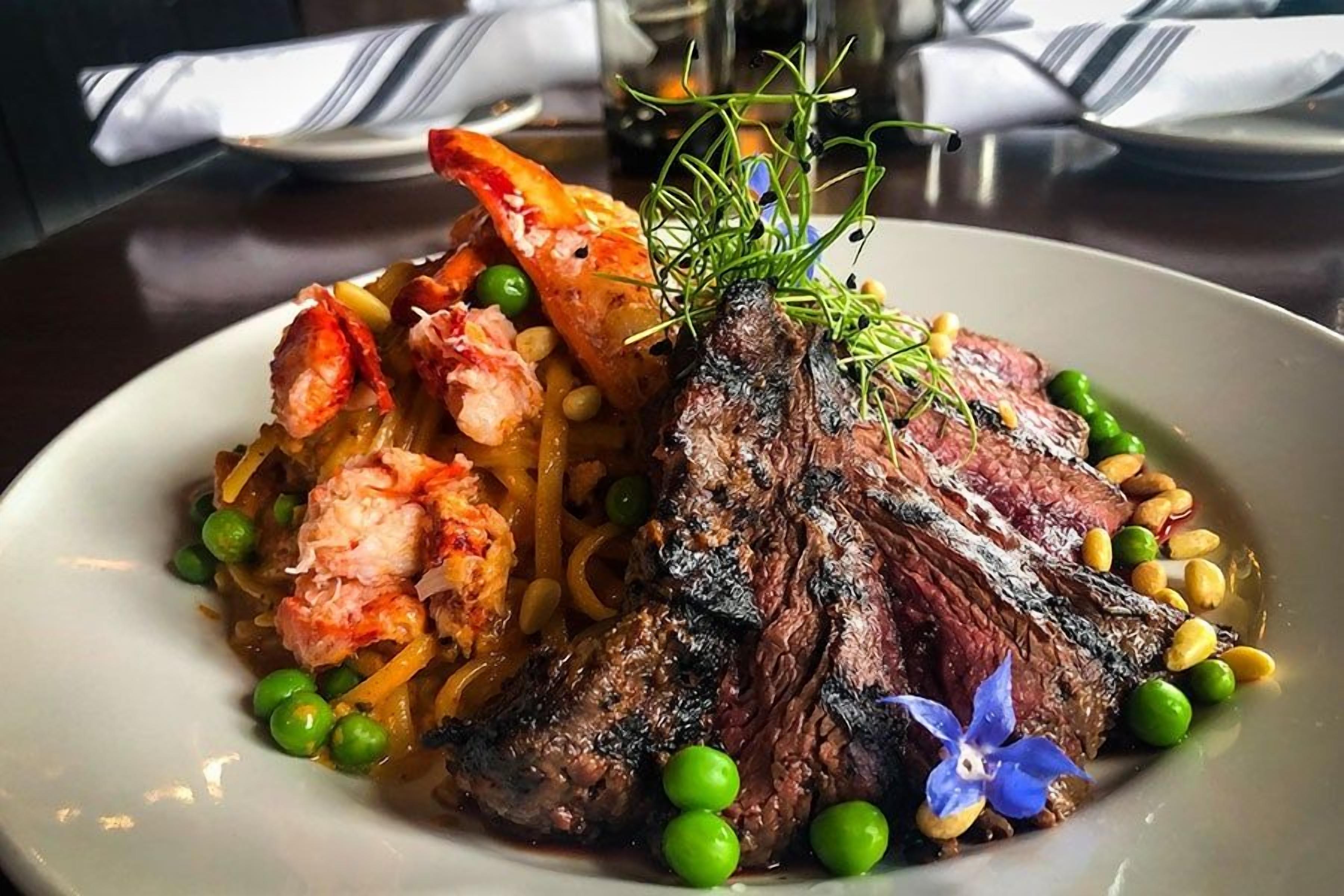A plate of food with a steak, lobster, peas, and a decorative flower.