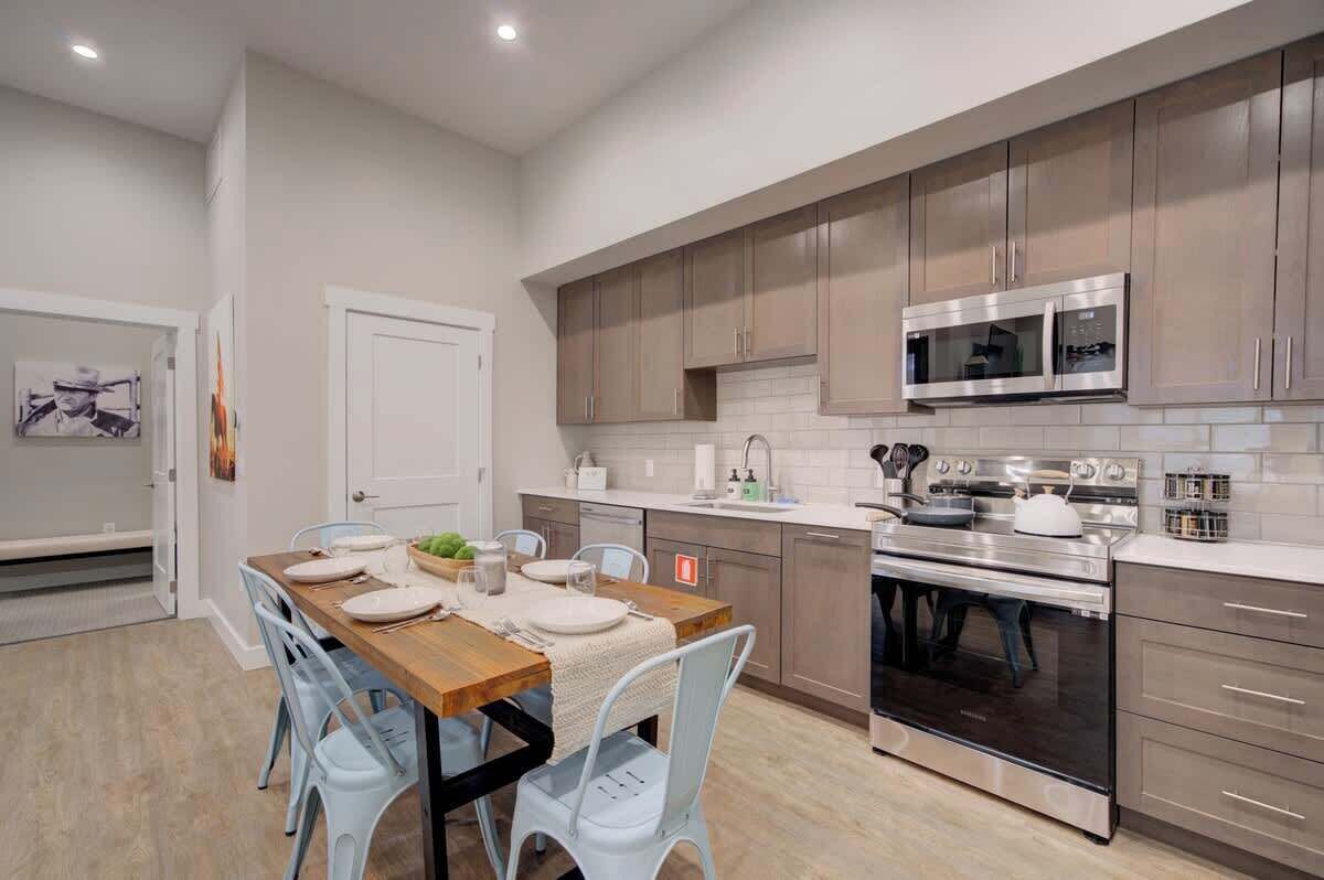 Una cocina moderna con electrodomésticos de acero inoxidable, armarios de madera clara y un comedor con mesa de madera y sillas azul claro.