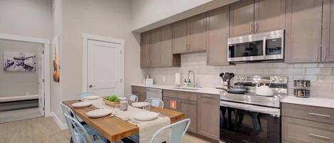 Una cocina moderna con electrodomésticos de acero inoxidable, armarios de madera clara y un comedor con mesa de madera y sillas azul claro.