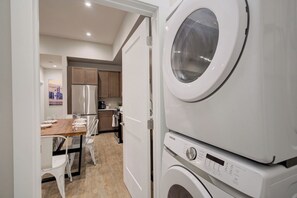 A compact kitchen with a built-in washer and dryer, a dining area with a table and chairs, and wooden cabinets. - Concrete Cowboy | Downtown Luxury Livin' (Bozeman)