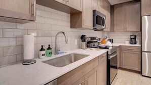 Une cuisine moderne avec des meubles de couleur bois clair, un réfrigérateur en acier inoxydable, un four à micro-ondes et un évier avec un robinet.