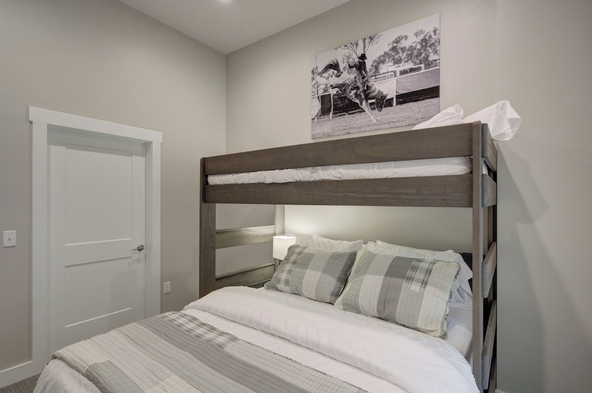 Uma cama beliche com encosto, uma porta branca e um quadro fixado na parede.