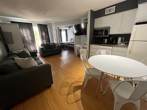 Un espacio habitable compacto con sofá, mesa de comedor, sillas, televisor de pantalla plana, electrodomésticos de cocina y una ventana con cortinas.