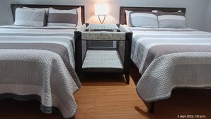 A hotel room with two beds, a nightstand with a lamp, and a view of a distant structure.