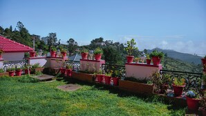 A residential area with houses, a red-roofed building, and a view of a mountain range. - Astha Home Stay (Kodaikanal)