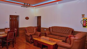 A room with a wooden dining table, two brown leather sofas, and a wooden coffee table. - Astha Home Stay (Kodaikanal)