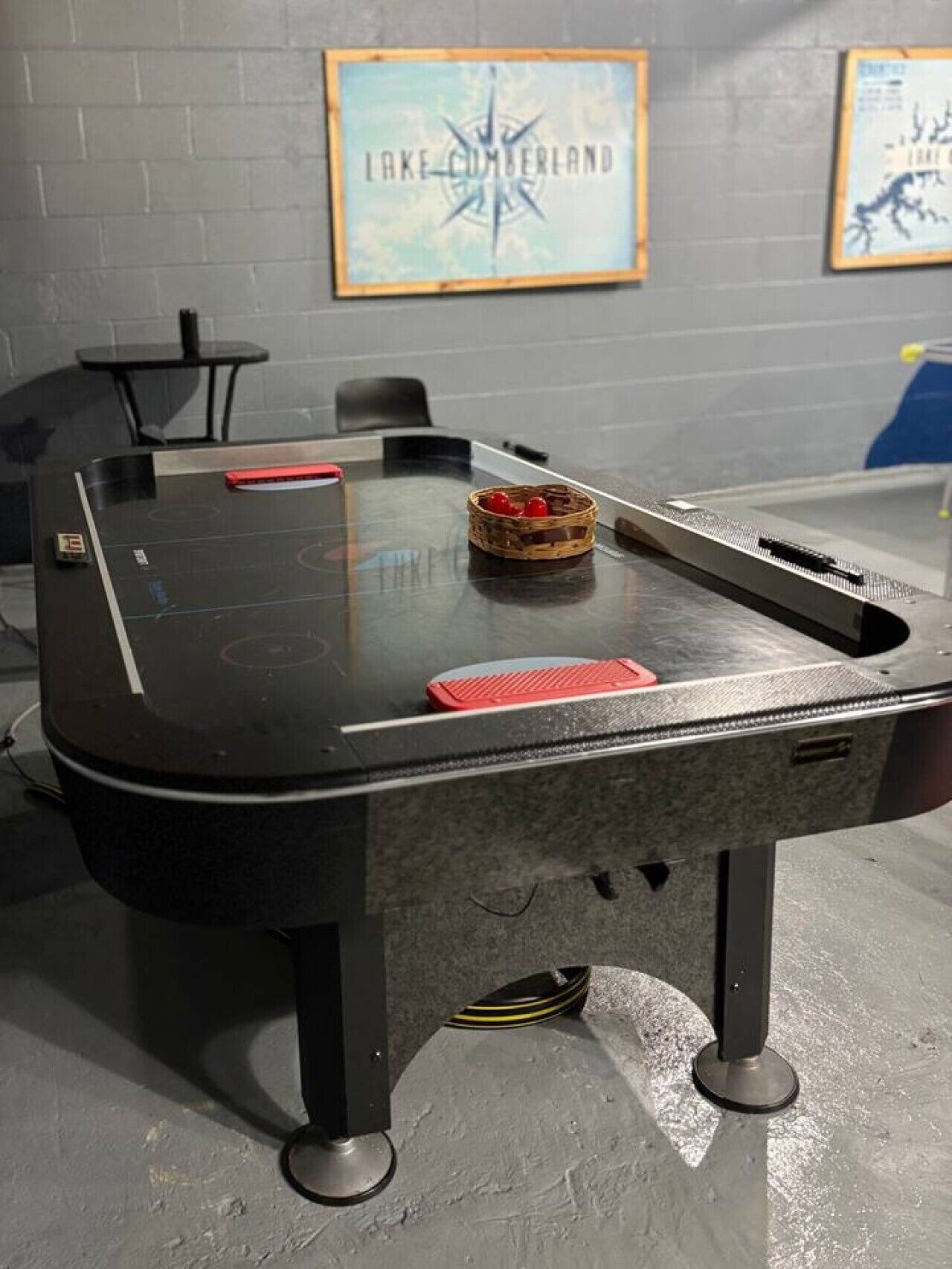 A table with a glass top, a basket with red objects, and a sign on the wall reading 'LAKE CUMBERLAND'.