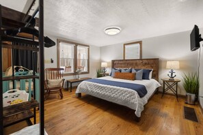 Un dormitorio con cama, una silla, una mesita de noche, una lámpara y una ventana.