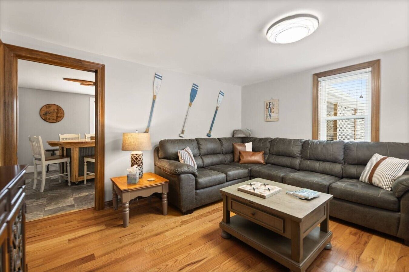 Un salon comprenant un canapé d’angle, une table basse, une lampe et un coin repas avec une table et des chaises.