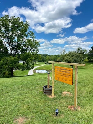 Señal de Lake Cumberland Stays & Events que muestra claramente un área verde, un sendero y una masa de agua al fondo.