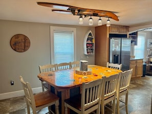 Un comedor con una mesa y sillas de madera, una lámpara decorativa en el techo y una cocina al fondo.