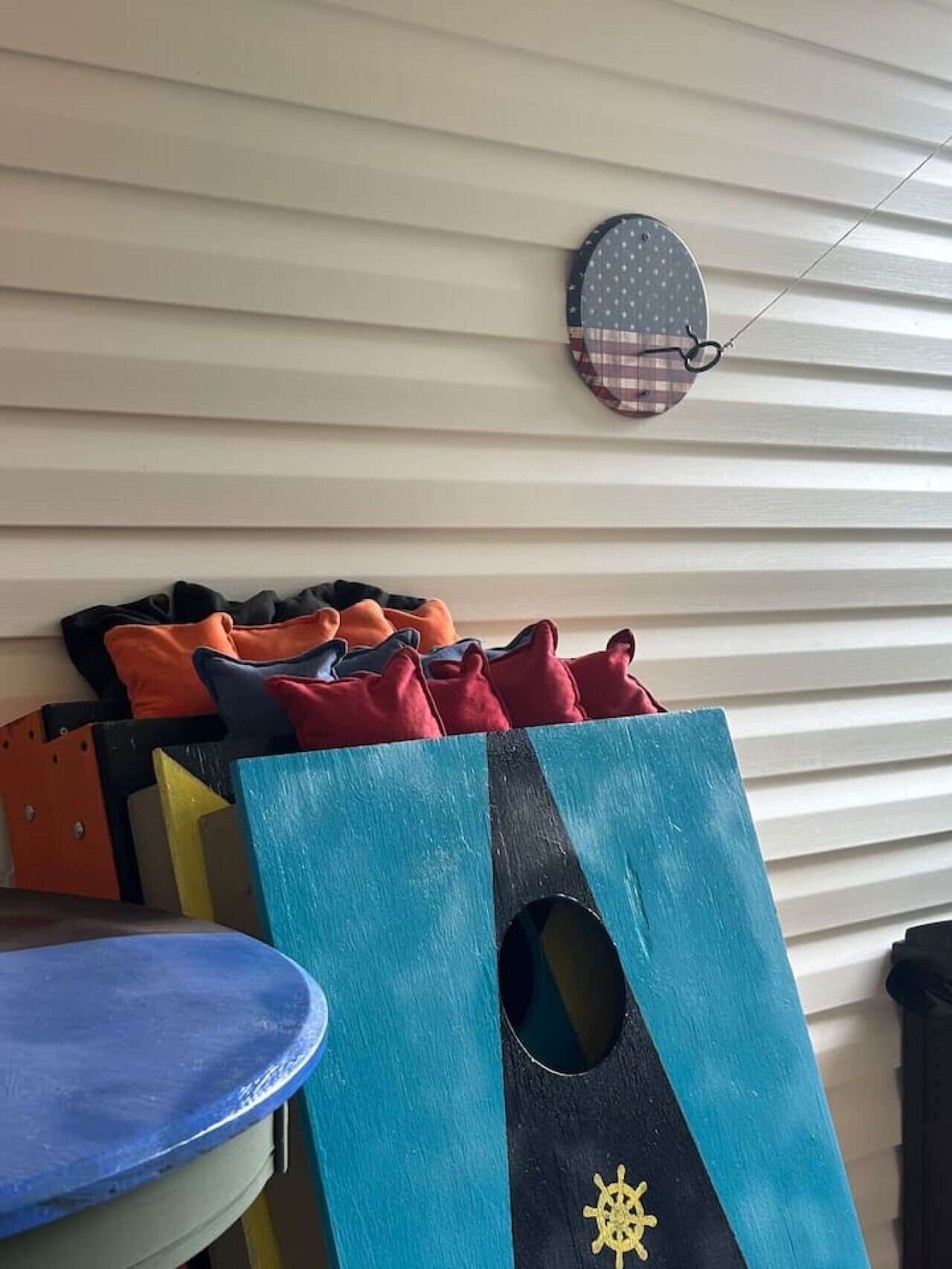 Un espace de rangement contenant divers objets, notamment un récipient bleu, un sac bleu et noir orné d’un motif de gouvernail de navire, et plusieurs coussins de couleurs vives.