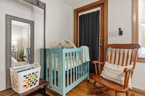Una habitación con una cuna, una mecedora, un espejo y una puerta con cortinas.