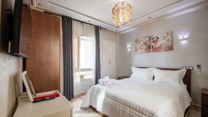 Hotellihuone, jossa on sänky, työpöytä kannettavalla tietokoneella, vaatekaappi ja suuri ikkuna, jossa on verhot.