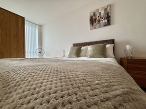 Un lit bien fait, avec une couverture à motifs, une tête de lit en bois et une table de chevet surmontée d’une lampe.