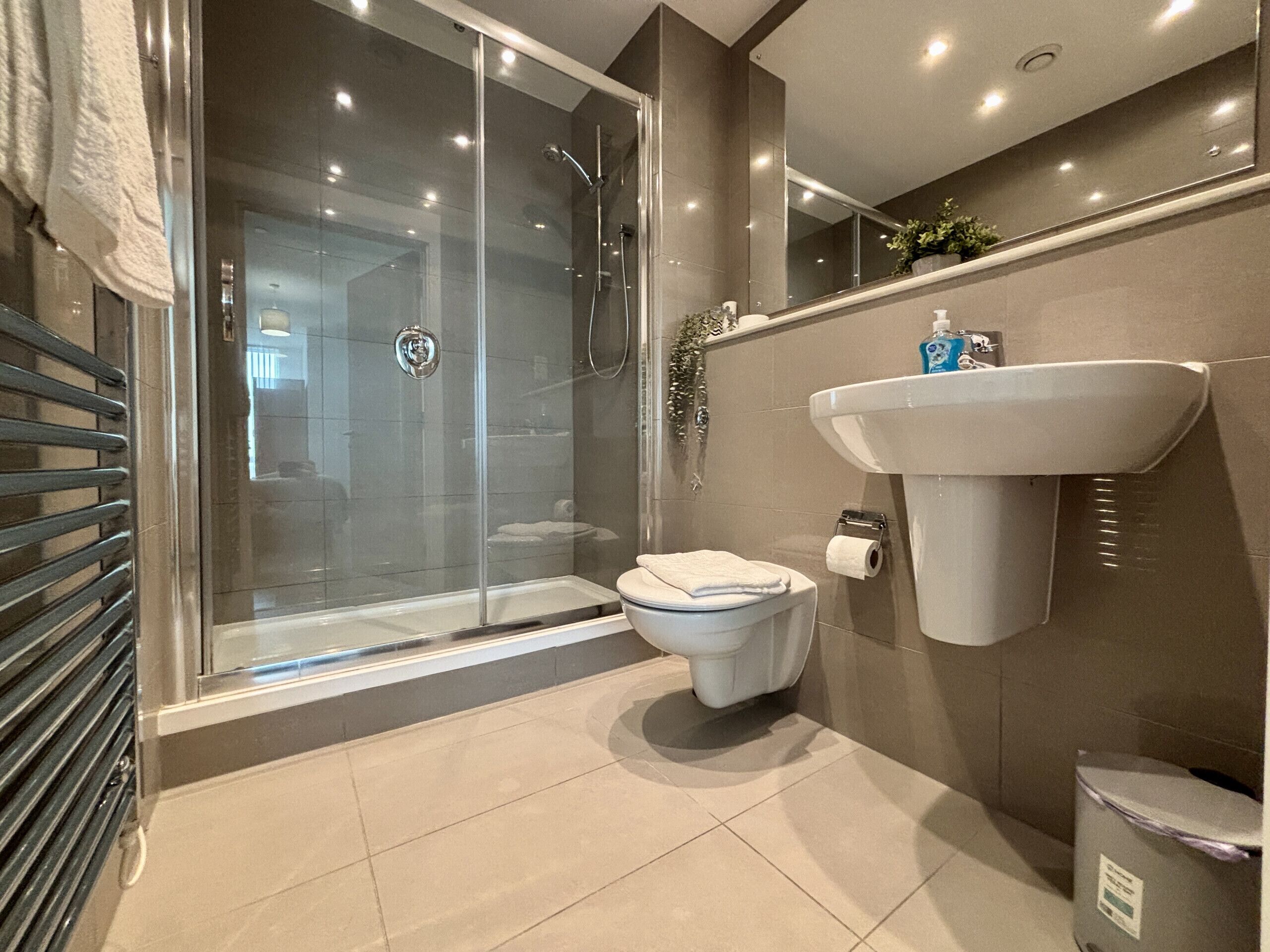 Ein modernes Badezimmer mit einer Glaskabine zur Dusche, einer weißen Toilette und einem an der Wand montierten Waschbecken.