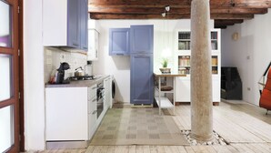 A compact kitchen with white cabinets, a blue door, and a stone column. - Spacious apartment in Venice (Venezia)