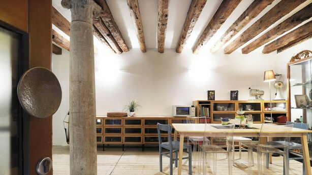 A room with exposed wooden beams, a wooden table with chairs, a television, and a bookshelf. - Spacious apartment in Venice (Venezia)