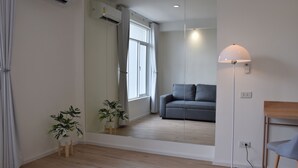 A modern living room with a grey sofa, a floor lamp, and two potted plants. - Squirrel House (Bangkok)