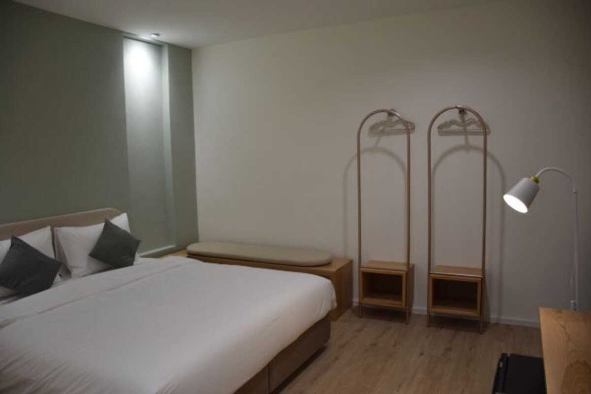 Une chambre à coucher comprenant un lit, des tables de chevet, un banc et un luminaire suspendu.