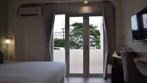 A hotel room with a bed, a desk, a chair, a TV, and a sliding glass door leading to an outdoor area. - Squirrel House (Bangkok)