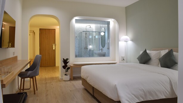 A modern hotel room with a large bed, a desk with a chair, a bathroom with a glass shower enclosure, and a large window. - Squirrel House (Bangkok)