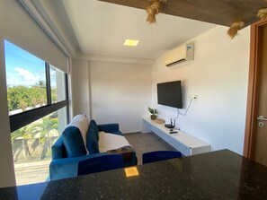A modern living room with a large window, a flat-screen TV mounted on the wall, a sofa, and a small table with a plant.