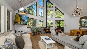 A spacious living room with a fireplace, large windows, and a high ceiling.