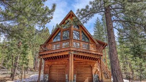 A wooden cabin with a balcony, two garage doors, and a staircase leading to the upper level.