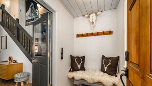 A cozy entryway with a wooden bench, two decorative pillows with antler designs, a mounted cow skull, and a staircase leading to another room.