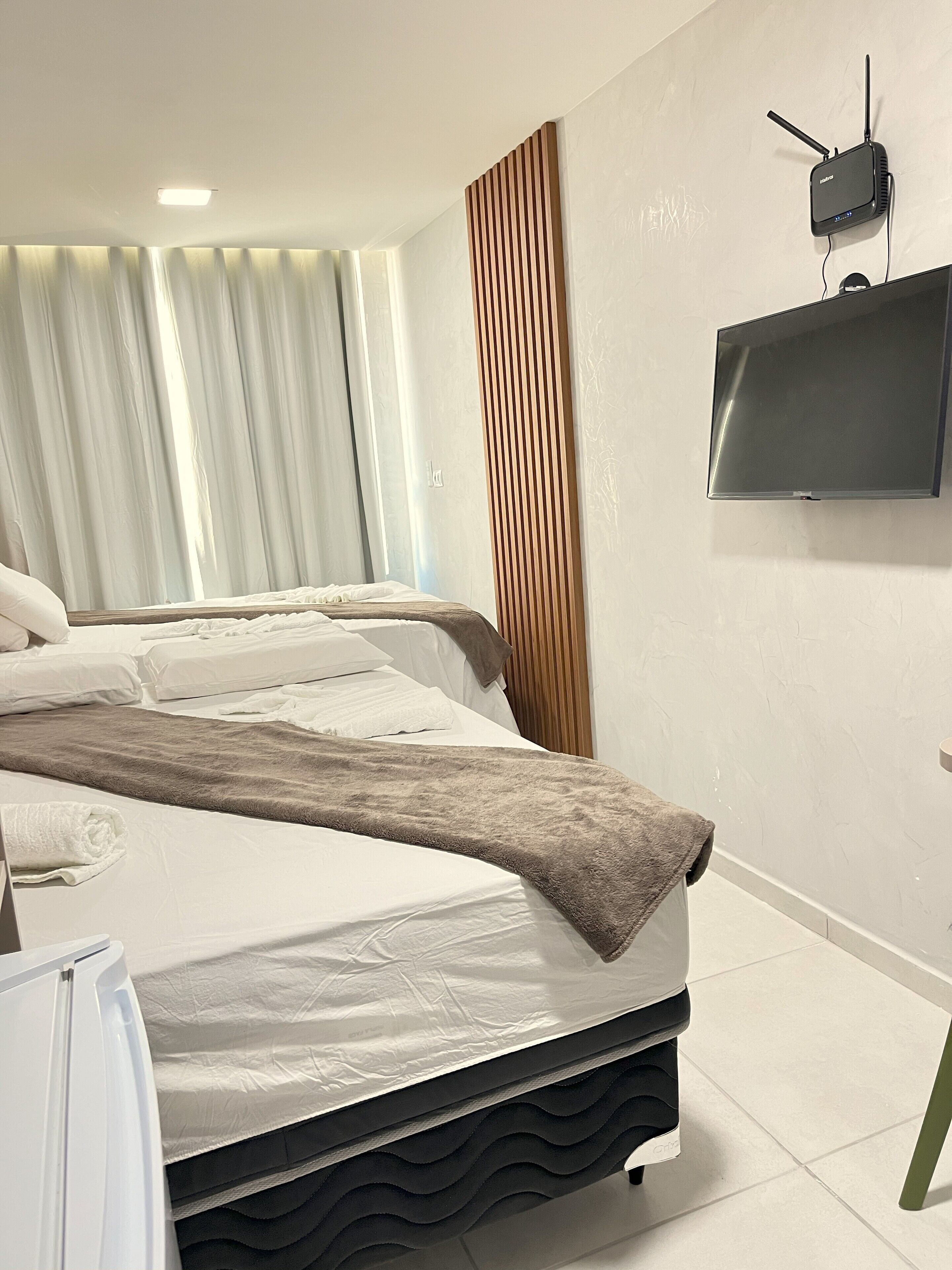 A hotel room with two beds, a flat-screen TV mounted on the wall, and a window with curtains.