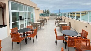 An outdoor patio with tables and chairs, a building with large windows, and a view of the sky. - Eco Mirage Residence by Easy Home (Ipojuca)
