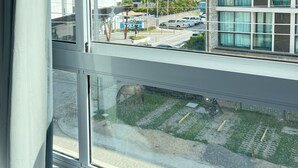 A view through a window of a building with a parking lot and other buildings in the background. - Eco Mirage Residence by Easy Home (Ipojuca)