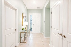 Un pasillo con puertas blancas, una consola de vidrio con una lámpara y un cuadro en la pared.