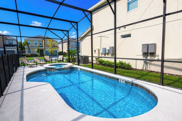 Una piscina con cerramiento de vidrio, sillas de descanso y vista a edificios residenciales.