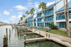 Un hôtel situé au bord de l’eau, doté de nombreux balcons, d’un quai et de palmiers.