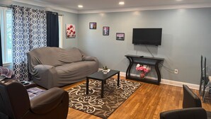 Un salon avec un canapé gris, une table basse, un téléviseur posé sur un meuble et un tapis à motifs.