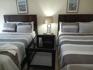 Ein Hotelzimmer mit zwei Betten, einem Nachttisch mit Lampe, einem Sessel und zwei gerahmten Bildern an der Wand.