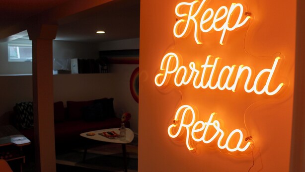 A neon sign with the text "Keep Portland Retro" in a room with a red couch and a small table.