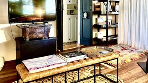A cozy living room with a wooden ceiling, a television, a bookshelf, and a patterned rug. - 2br Historic Adobe - 2acr Homestd A/C Exquisite NEW to VRBO! (Santa Fe)