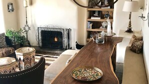A cozy living room with a wooden dining table, a fireplace, a bookshelf, and a sofa. - 2br Historic Adobe - 2acr Homestd A/C Exquisite NEW to VRBO! (Santa Fe)