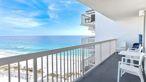 Un balcón con vista al océano, muebles blancos y barandilla.