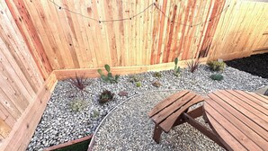 A wooden deck with a table and chairs, surrounded by a wooden fence and various plants. - New! 4BR Vacation Home, Tub, BBQ, EV, close to Sequoia (Visalia)