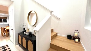 A modern staircase with a wooden finish, a black console table with decorative items, and a white wall with a round mirror. - New! 4BR Vacation Home, Tub, BBQ, EV, close to Sequoia (Visalia)